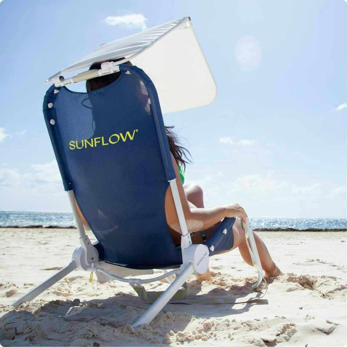 Person sitting on a beach in a dark blue Sunflow chair with the sun shining in the background