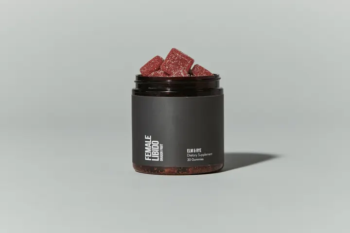 An open jar of Elm & Rye Female Libido gummies, piled high with red gummies, on a pale gray backdrop