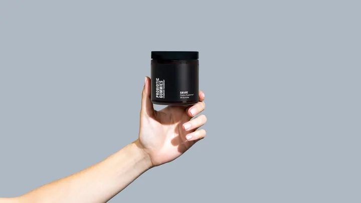 A hand holds up a jar of Elm & Rye Probiotic Gummies against a blue-gray backdrop