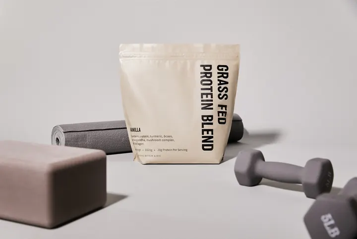 A pouch of Elm & Rye Grass Fed Protein Blend with a yoga mat, a yoga block, and 2 dumbbells