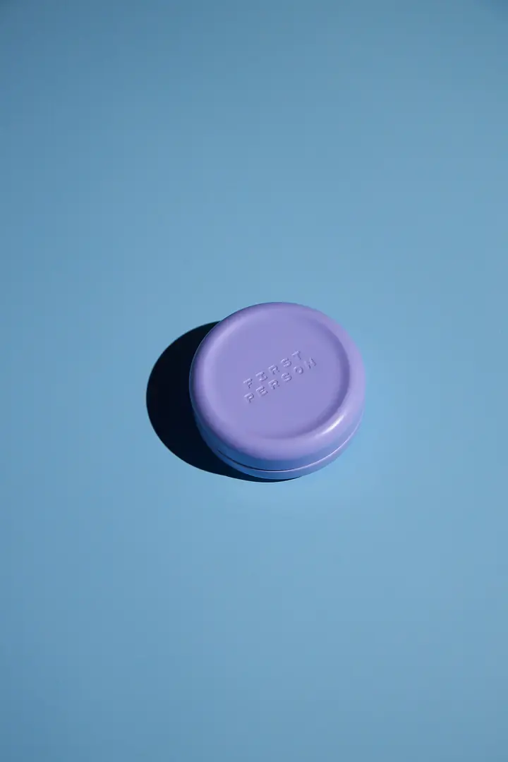 A lavender First Person Moonlight tin on a blue backdrop