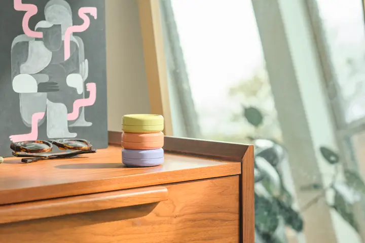 3 First Person supplement tins stacked on a walnut dresser beside a bright window
