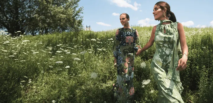 2 models in Mestiza floral and green print dresses walking through a summer meadow