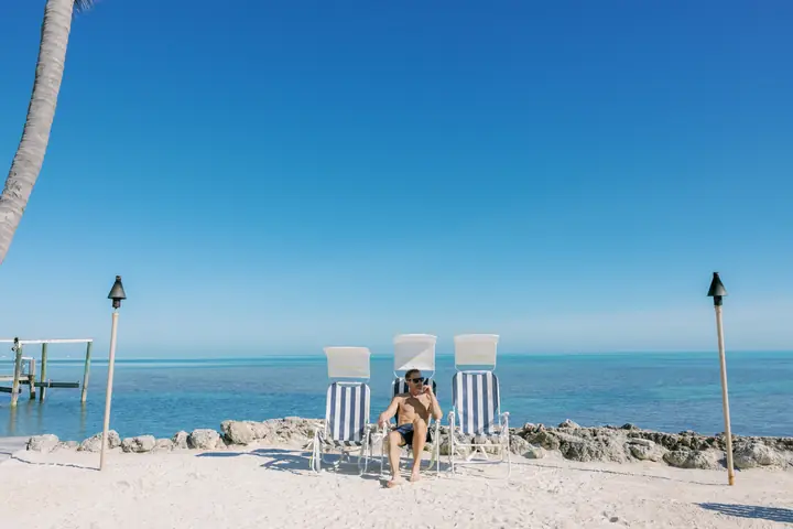 A man relaxes among 3 striped Sunflow chairs on a rocky shore beside a dock