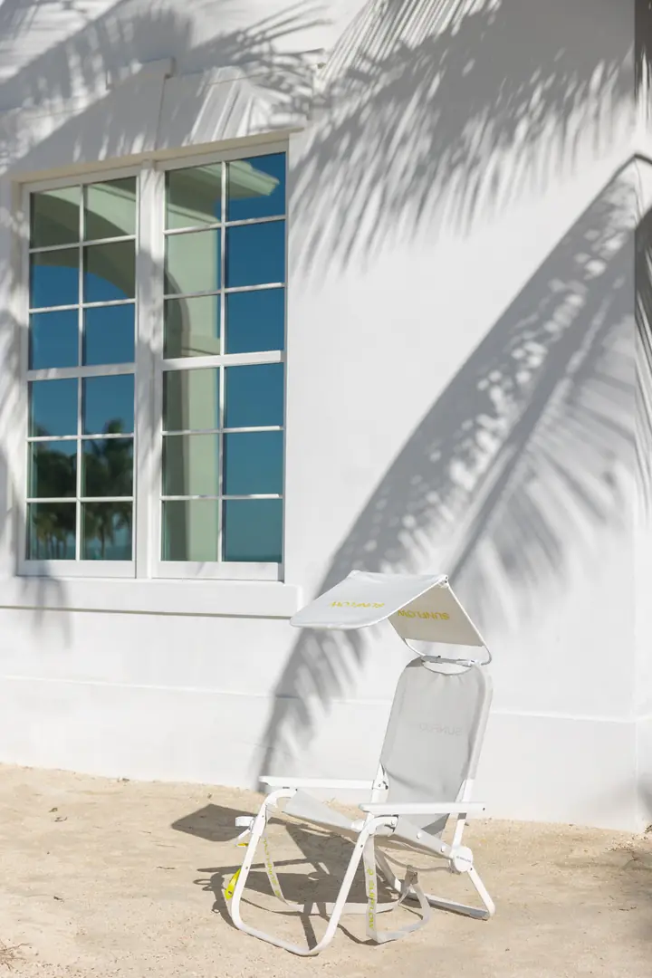 A white Sunflow beach chair with its sun shade against a white wall striped with palm shadows