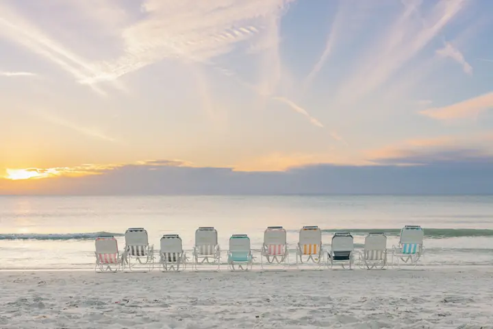 A row of Sunflow beach chairs facing the water at sunset