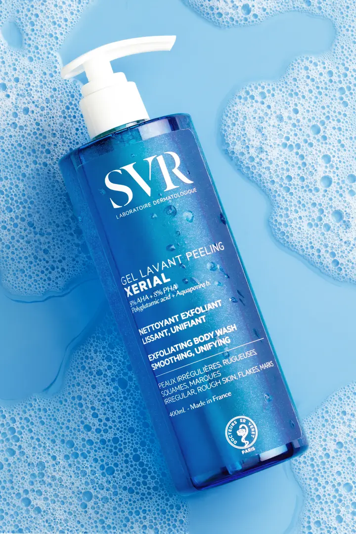 A bottle of SVR Xerial exfoliating body wash lying in blue foam