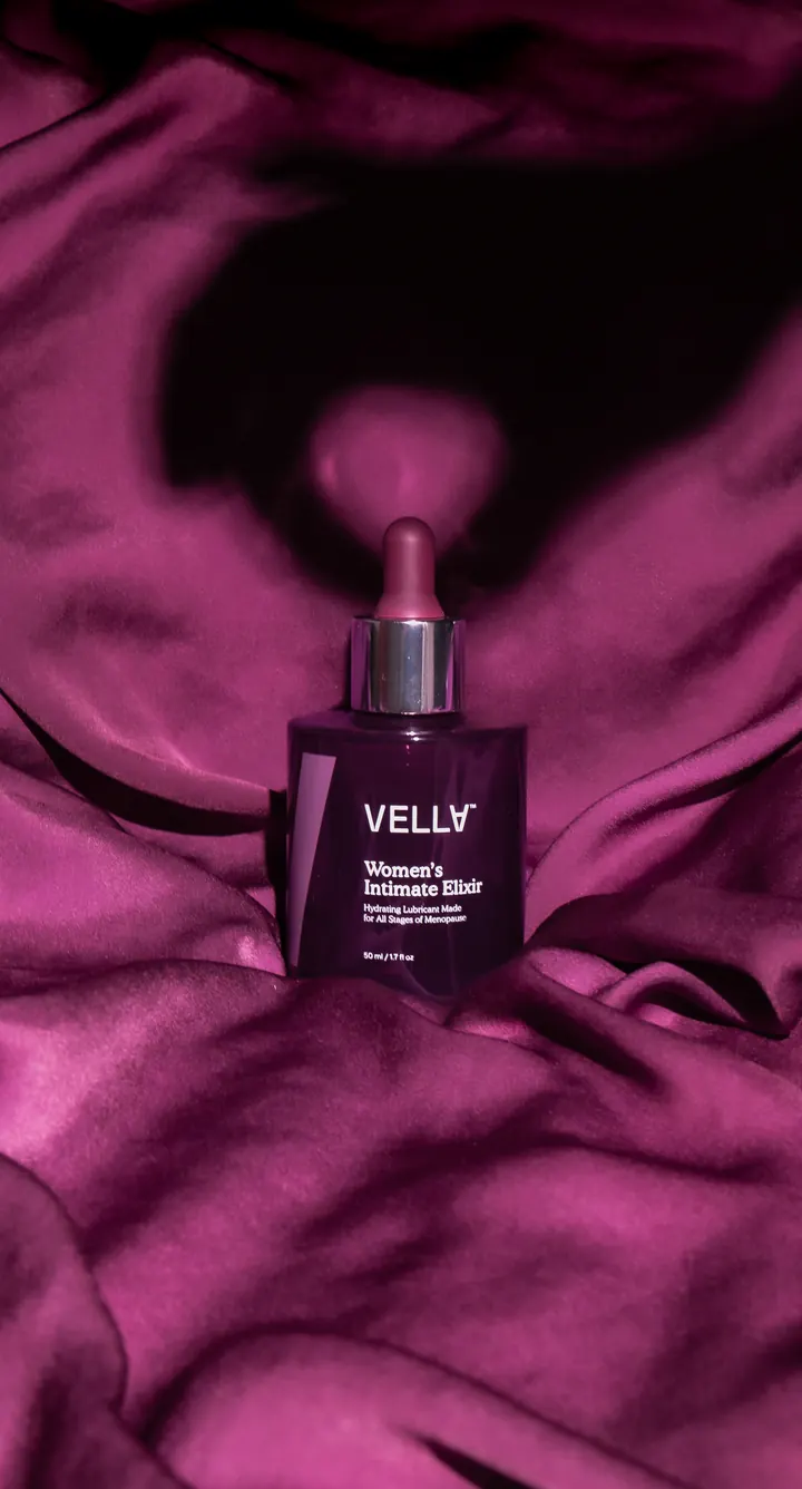 A bottle of Vella Women’s Intimate Elixir resting in folds of magenta satin
