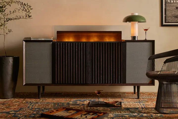 A Wrensilva record console with its lid glowing, next to a lamp and a cocktail on a Persian rug